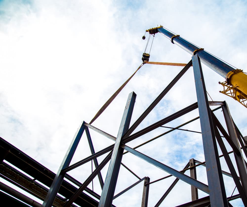 Crane lifting steel framing components at a construction site
